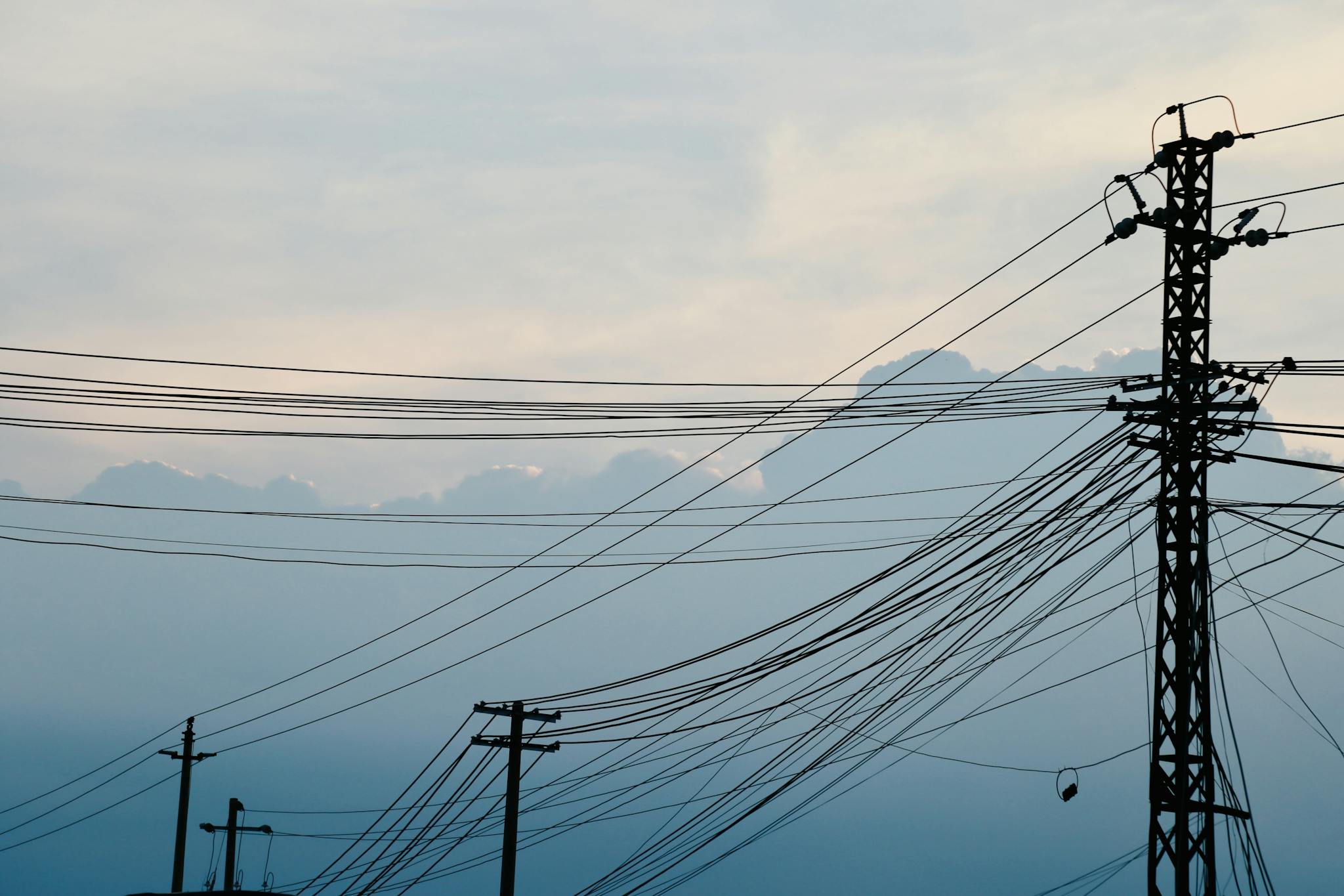 Silhouetted power lines and poles with clouds and sky background, serene atmosphere.